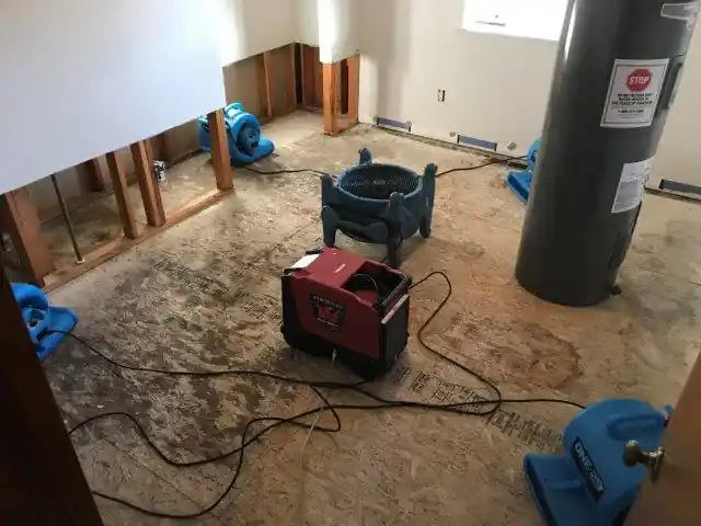 Basement with carpet pulled up, a red dehumidifier and blue air movers drying the floor