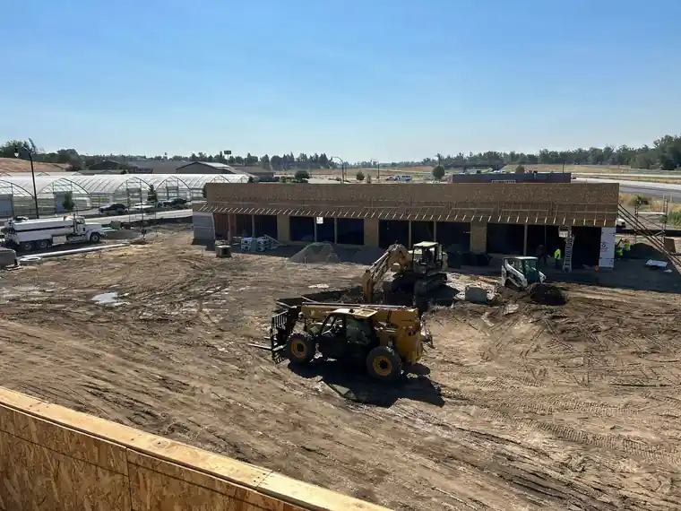 A commercial site under grading, with a telehandler and building shells behind.
