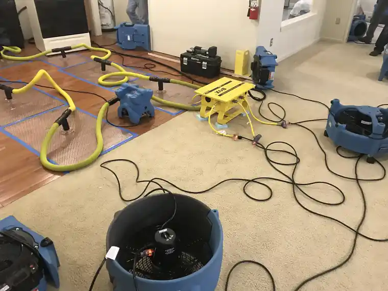 Air mover, hoses and a dehumidifier drying a kitchen floor on a water damage job