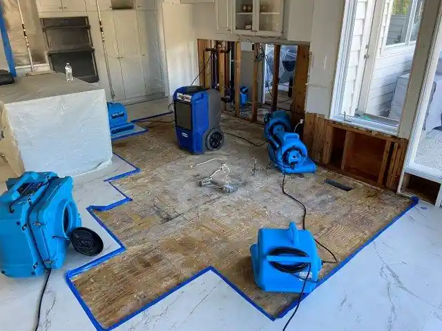 Kitchen floor cut out to the subfloor, taped off, with air movers set.