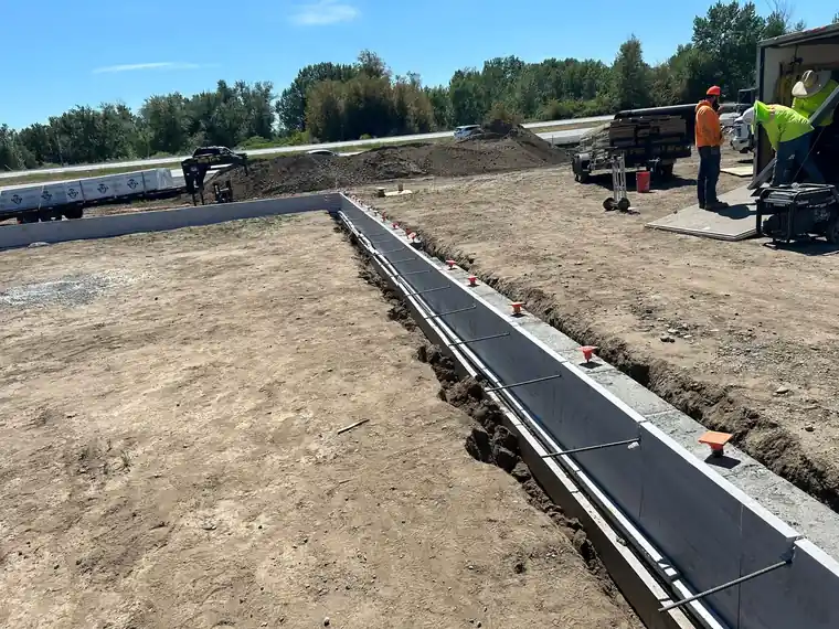 Crew setting a concrete footing, two workers in hi-vis.