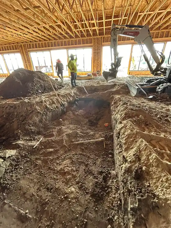 An excavator and two workers inside a framed building.