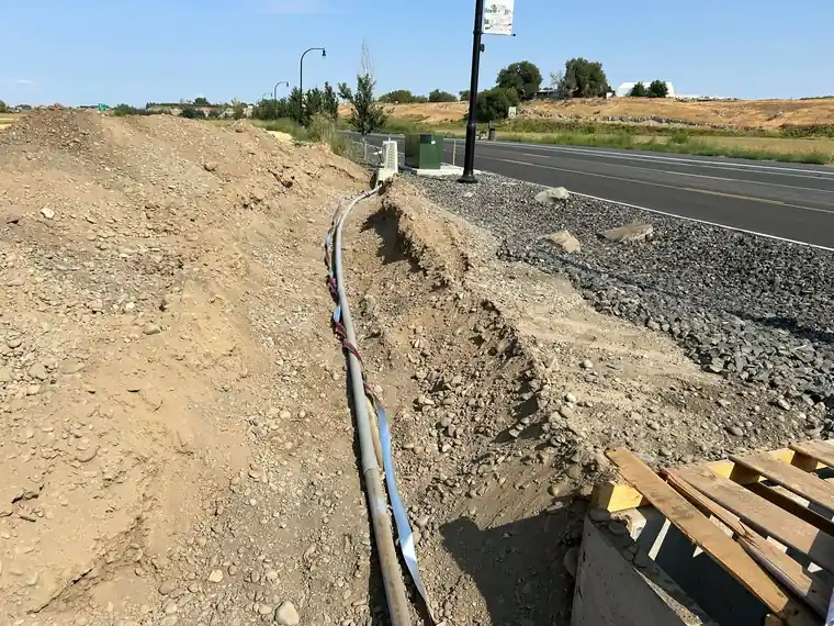 Utility trench with conduit along a roadway, valley hills behind.